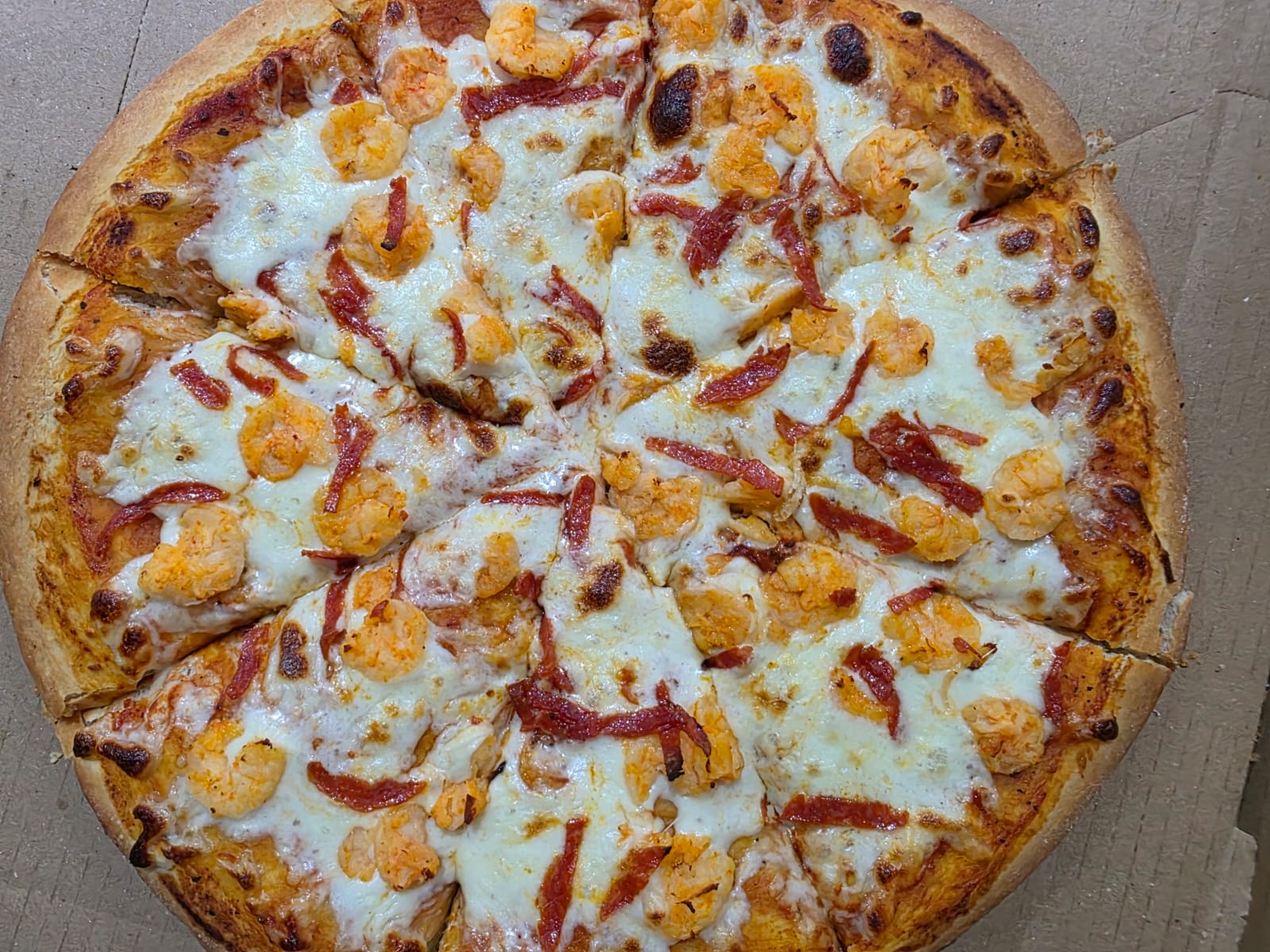 Pizza de Pizza Sur con camarones y tiras de pepperoni sobre queso fundido